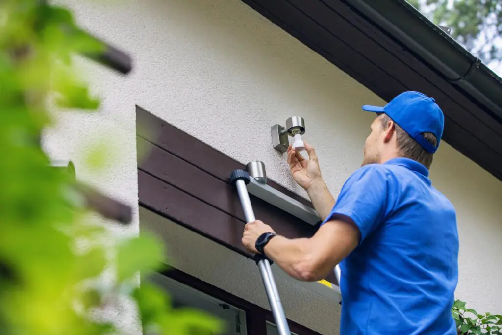 Outdoor lighting installation process showing a technician screwing in an exterior wall light